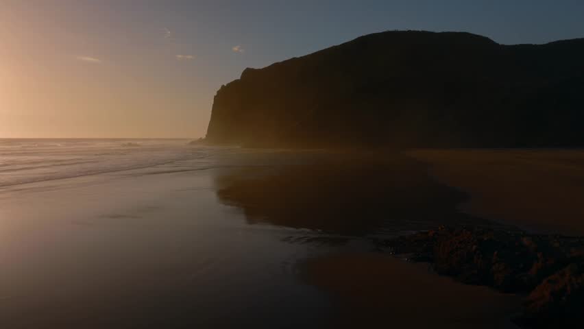 Sandy beach and calm ocean waves at sunset. Anawhata, Piha, Auckland, New Zealand.