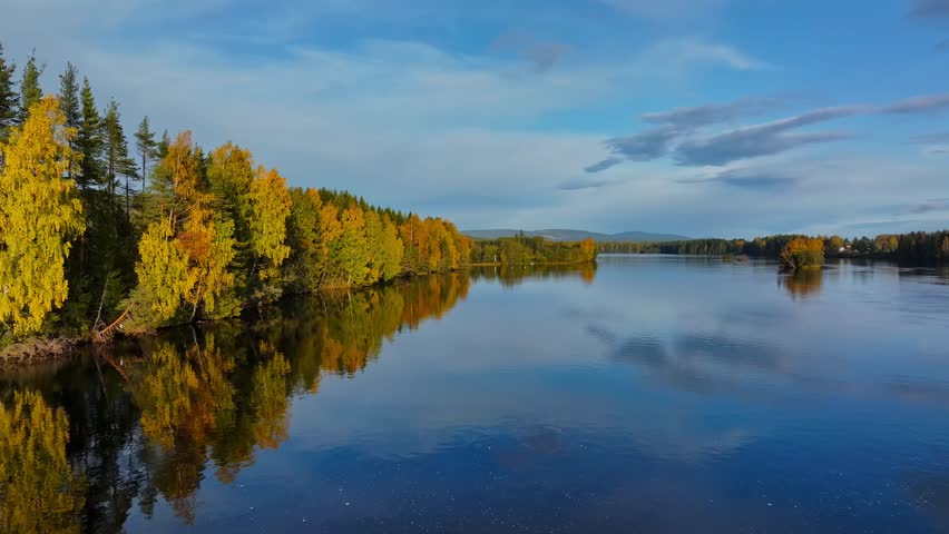 A drone footage over a tranquil lake in a forest with visible reflection on the water surface of the autumn trees under blue sky on a sunny day - Powered by Shutterstock - Get 15% off with code: PIKWIZARD15