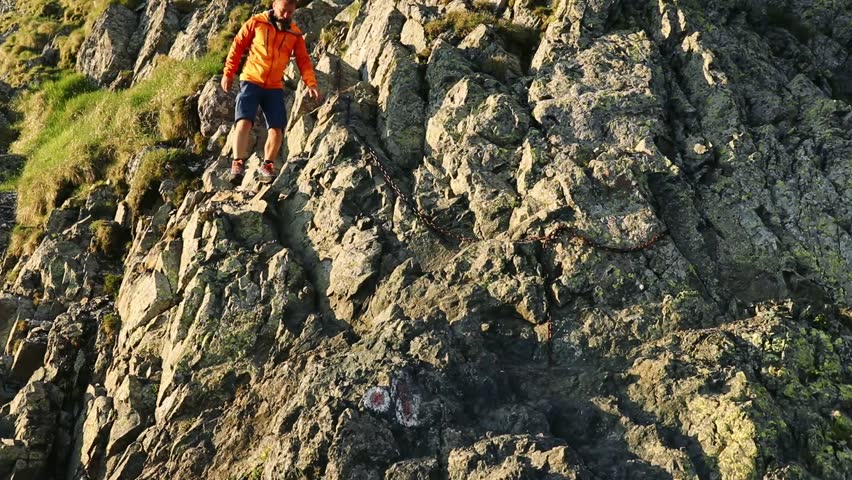 A man in sportswear climbing the rocky mountain on a sunny day