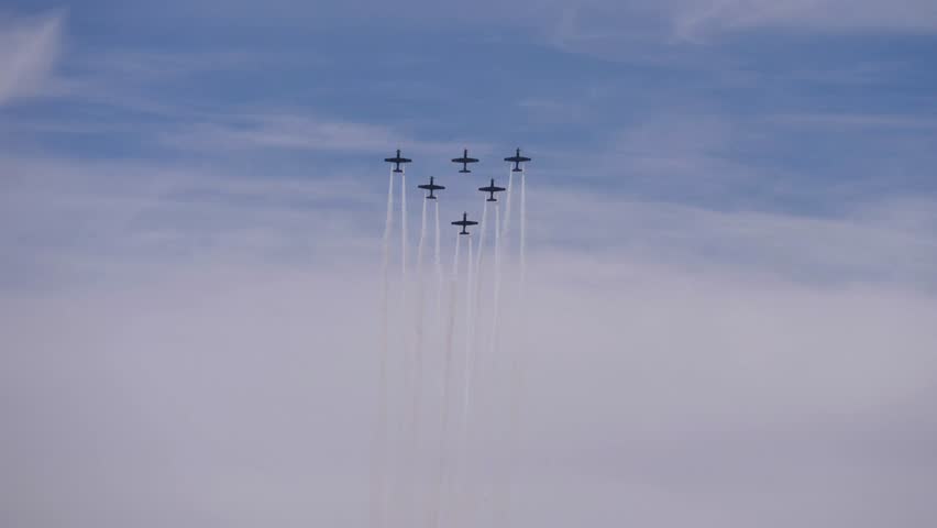 A group of military planes emit white gases and fly at great speed in the blue sky
