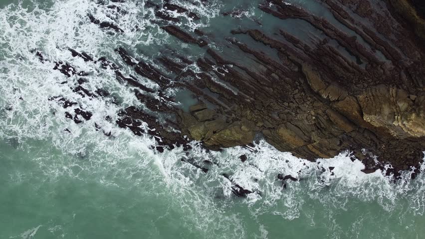 An aerial top view video of sea waves crashing on the shore covered with buildings