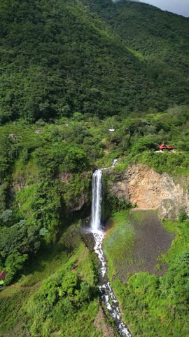 vertical erial drone view of the Manto de la Novia waterfall in Baños de Agua Santa, Tungurahua, Ecuador, where the cascading water creates a beautiful rainbow