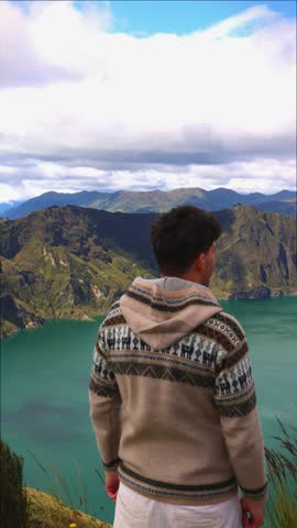 vertical young person viewed from behind, gazing at the stunning Quilotoa Lagoon in the Ecuadorian Andes. The scene highlights the beauty of the lagoon and the surrounding mountainous landscape