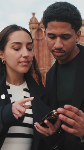 Vertical video, Two young people looking at smartphone together with blurred historical city background.