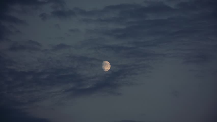 The moon moving through gray cloudy sky in the evening