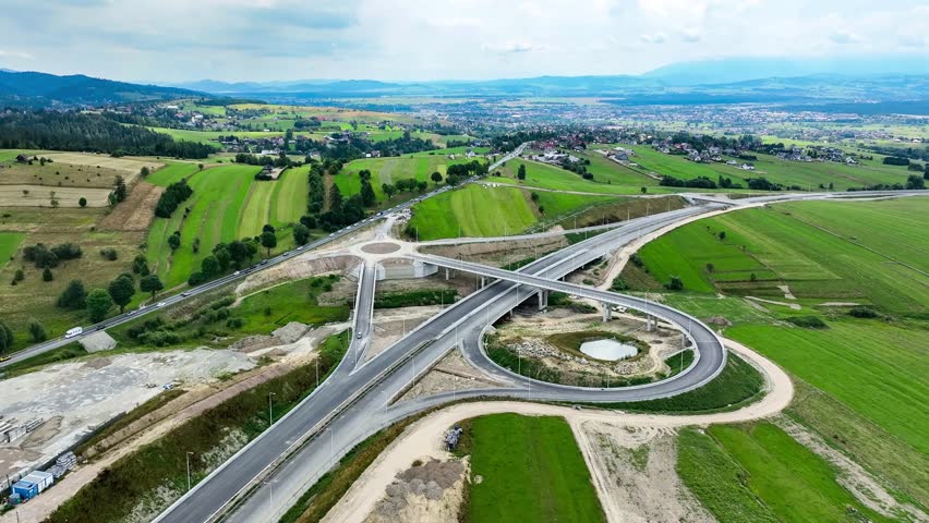 New fragment of highway under construction on Zakopianka road, Poland, clearing Nowy Targ town. Entrance, exit ramps, traffic circle. State in July 2024. Aerial view. Old road with traffic in the left