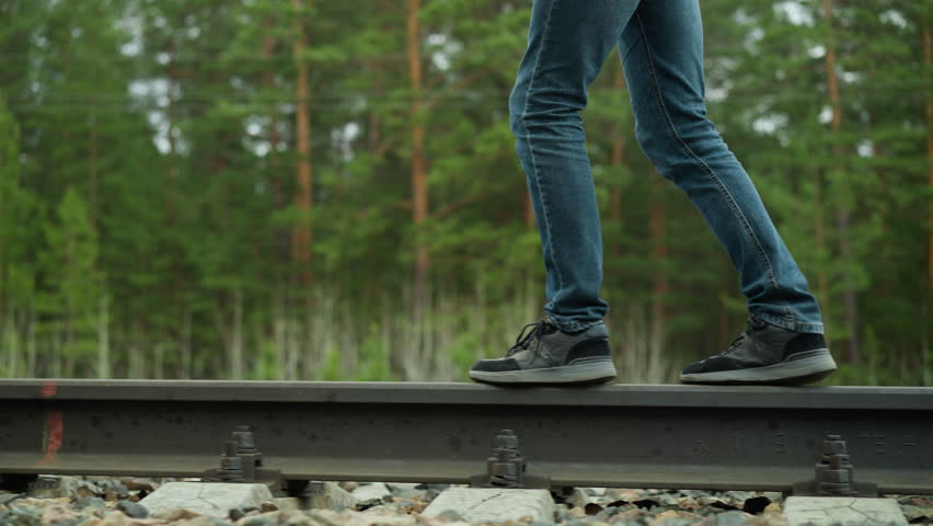 Close-Up of Person Walking on Railway Track in Blue Jeans and Black Sneakers