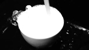 A closeup grayscale of a tap pouring and overflowing a white ceramic cup - Powered by Shutterstock - Get 15% off with code: PIKWIZARD15