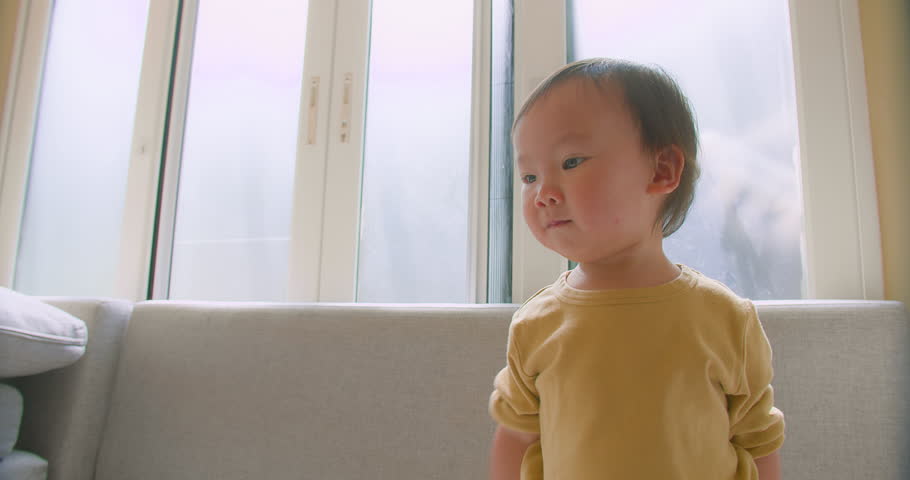 Portrait happy little cute Asian toddler child girl looking smiling and dancing jump having fun on sofa in living room at home