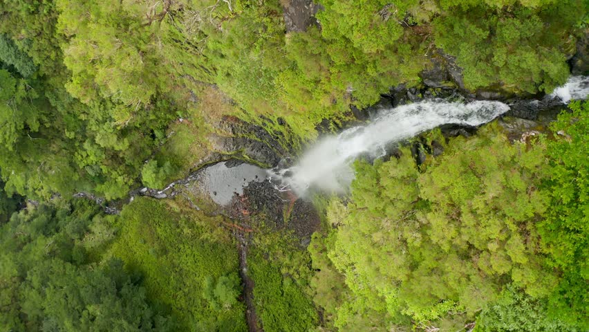 An aerial view of a flowing waterfall on the green mountains of Madeira Island