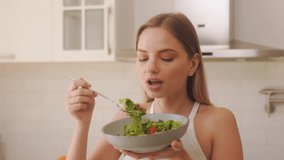 The woman is greedily eating salad in a modern kitchen. She is eating from a bowl filled with greens and cherry tomatoes, holding a fork in one hand and the bowl in the other. - Powered by Shutterstock - Get 15% off with code: PIKWIZARD15
