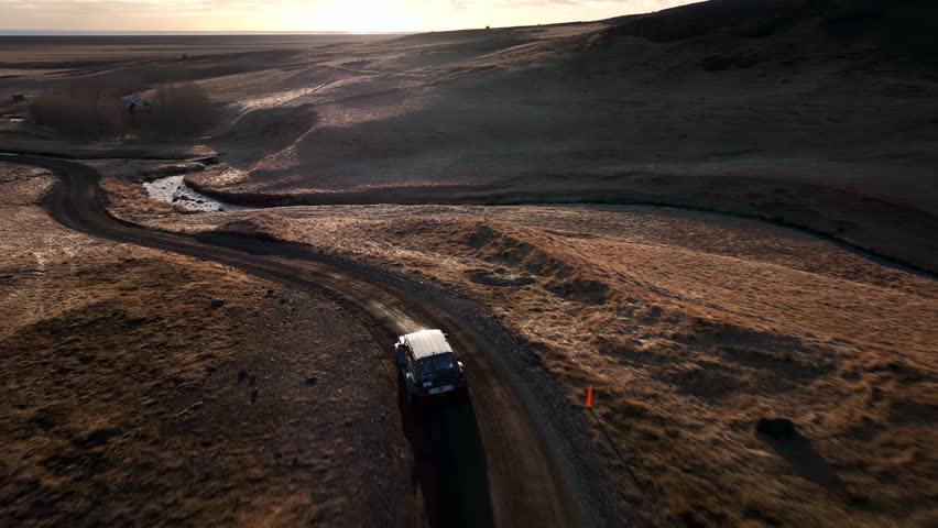 Aerial landscape view over a four wheel drive car, driving on a winding dirt off road track, in Iceland, at sunset