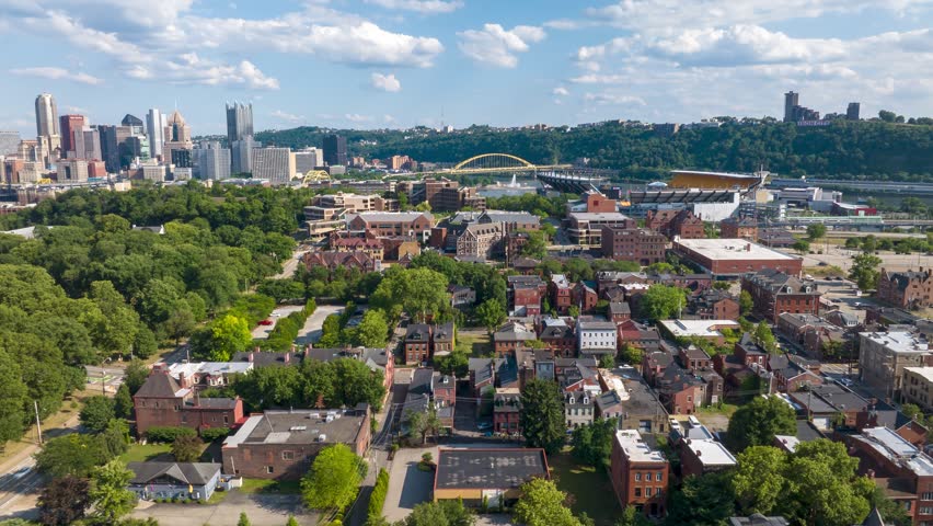 Pittsburgh skyline with downtown buildings and a large green park. Residential neighborhoods in the foreground. Allegheny River in the distance. Aerial hyper lapse of North Shore historic district.