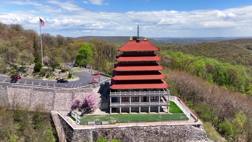 America flag and parking cars on top of Mount Penn. Pagoda Building during sunny day in spring. Aerial orbit shot.