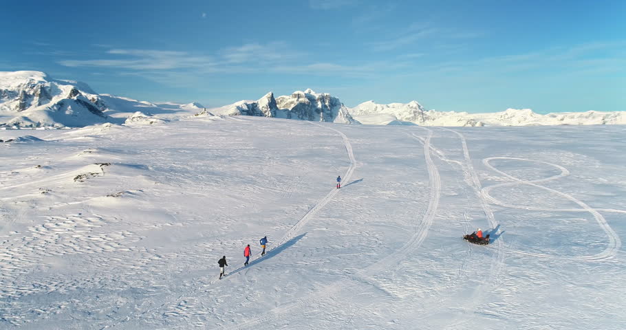 People enjoy outdoor sport activity in Antarctica. Group of scientists from polar station run snow trail race. Travel, active lifestyle, recreation in arctic wild nature landscape. Aerial drone shot