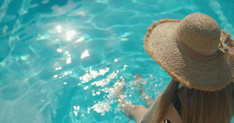 Young woman in a hat sitting at the edge of a pool, enjoying the coolness of the water