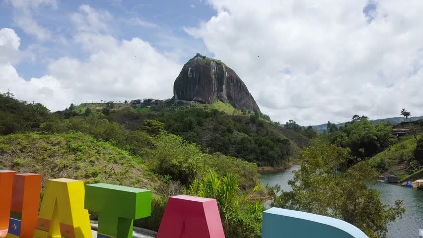 Stunning aerial view of The Rock of Penol in Guatape, Colombia, surrounded by lush greenery and serene water bodies. push forward shot