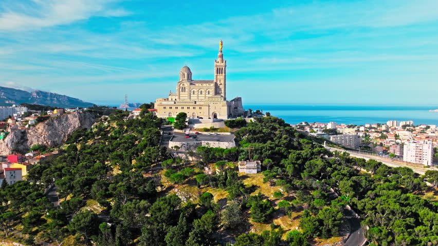 Grand basilica on top of a hill crowned by a golden statue, old city centre and port by blue Mediterranean sea coast in Marseille, France. Basilica of Notre Dame of la Garde at Marseille in France.
