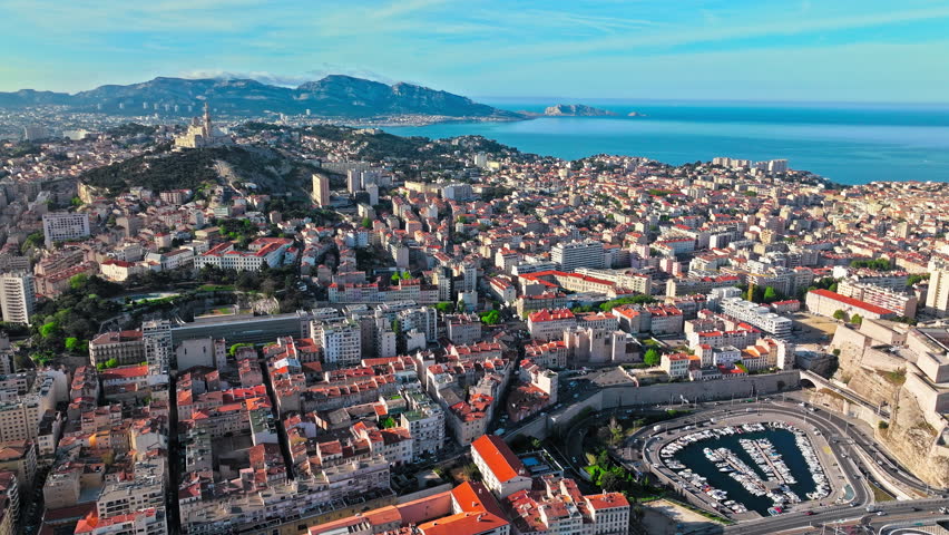Grand basilica on top of a hill crowned by a golden statue, old city centre and port by blue Mediterranean sea coast in Marseille, France. Basilica of Notre Dame of la Garde at Marseille in France.