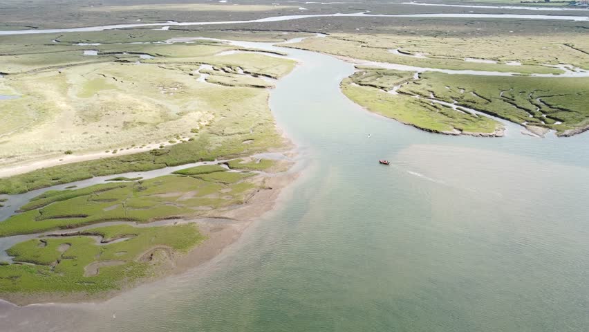 An aerial slow movement around sea surrounded by green fields with floating boat in Norfolk in 4K