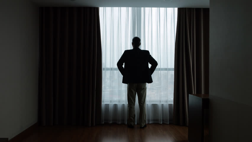 Standing at window, businessman in suit dramatically opens blackout curtains with single motion. In slow motion, his full-length silhouette is seen from behind, hands on hips in akimbo pose.