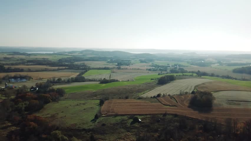 Aerial shot of expansive Wisconsin farmland featuring fields, patches of trees, and rolling hills under a clear sky.