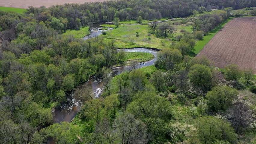 A lush, green landscape with a meandering river flowing through a forest and farmland in Wisconsin.