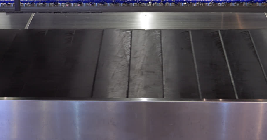 Close view of empty slat conveyor in baggage claim hall of airport. Black slats of typical luggage belt move quickly under dim lighting. No bags and no people are visible in this shot