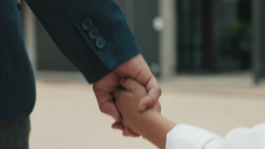 Strong hand of father holds tiny hand of schoolboy tightly. Loving father walks small son to school and listens attentively as boy in school uniform describes plans for weekend