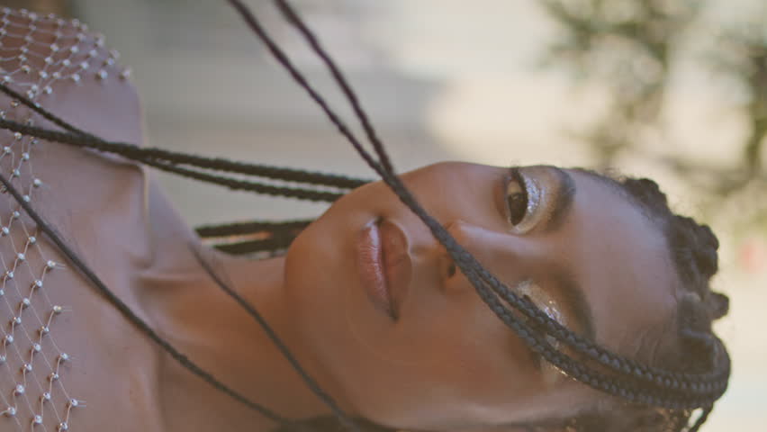 Afro braids girl posing windy street vertical portrait. Sensual dreadlocks brunette in trendy outfit looking camera alone closeup. Cosmic stylish woman enjoying summer breeze at sunshine square