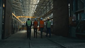 Back view of four heavy industry technicians in uniform and helmets discussing production process, walking at manufacturing plant. Male and female inspectors talk to employees in factory. Slow motion. - Powered by Shutterstock - Get 15% off with code: PIKWIZARD15