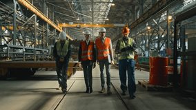 Four heavy industry engineers in safety uniform and hard hats discuss work process walking at manufacturing factory. Mature supervisor holds laptop, talks to diverse workers in warehouse. Slow motion. - Powered by Shutterstock - Get 15% off with code: PIKWIZARD15