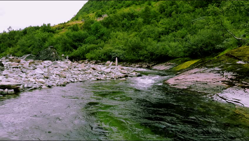 An aerial time-lapse footage of a river flowing in a lush forest in Norway