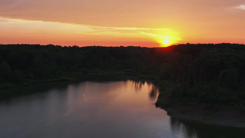 A beautiful sunset over a forest landscape and calm lake, aerial view
