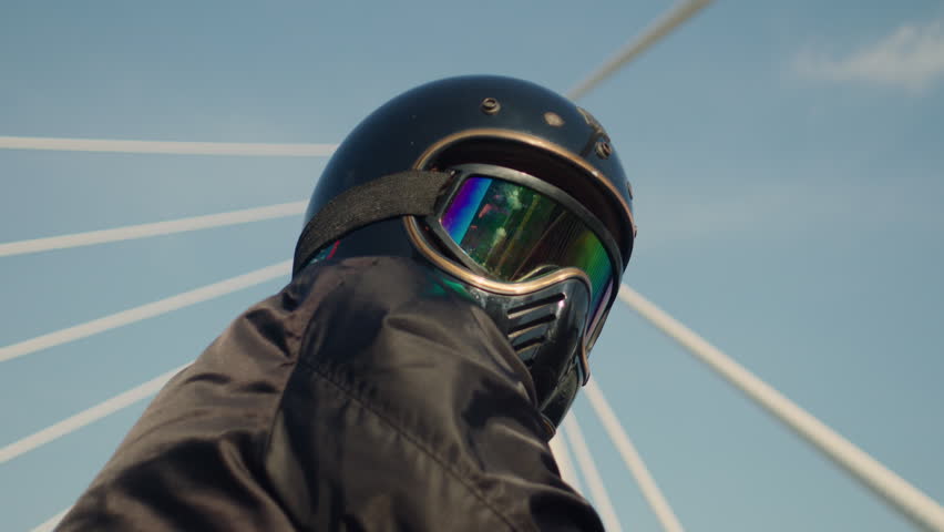 motorcycle rider wearing helmet and goggles riding on big iron bridge with clear sky, low angle slow motion 