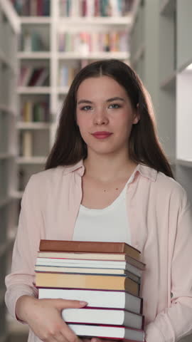 Woman with high books stack in university library. Brunette student holds scientific literature pile in bookstore. Brunette librarian in shop portrait