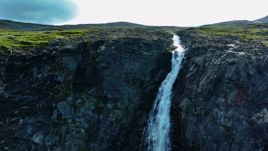 A landscape scene of a flowing waterfall through high rocky mountain