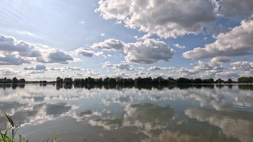 A scenic view of a tranquil lake with visible reflection of the clouds and plants on a sunny day