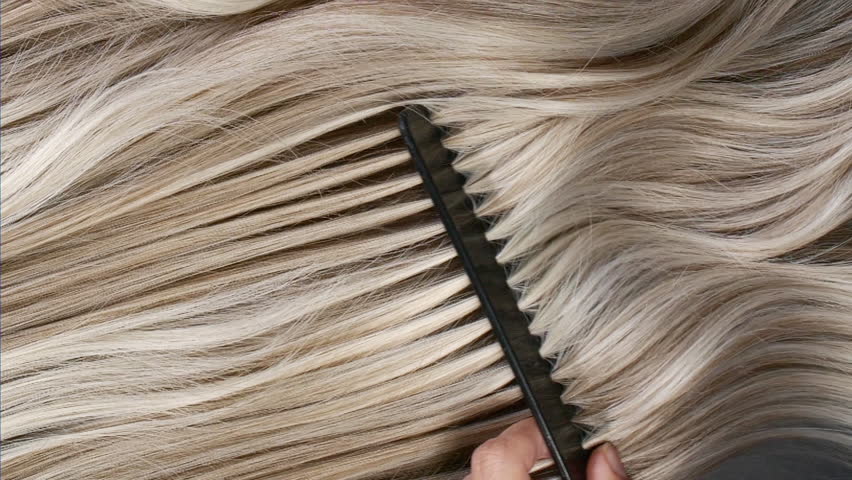 Closeup blond hair texture, slow motion of female hand combing long curly hair