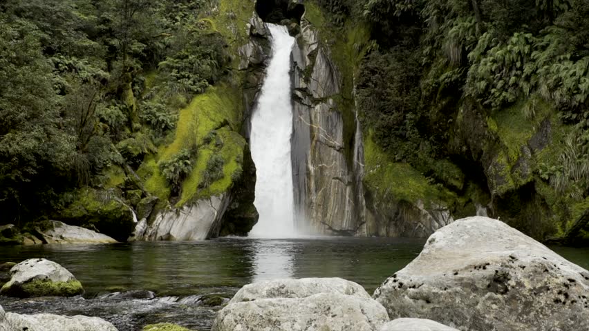 A waterfall on the Milford Track, New Zealand in slow motion pours into the river below it.