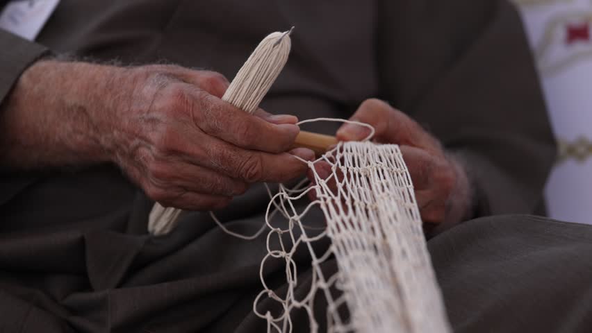 Senior man is knitting traditional fishing net, closeup on hands. High quality 4k footage.