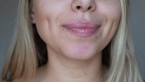 Young caucasian blonde woman applying a hygienic lipstick on her lips on a grey background. Moisturising chapstick for dry lips - Powered by Shutterstock - Get 15% off with code: PIKWIZARD15