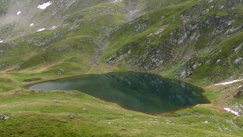 A small mountainous lake surrounded by green mountains during the daytime