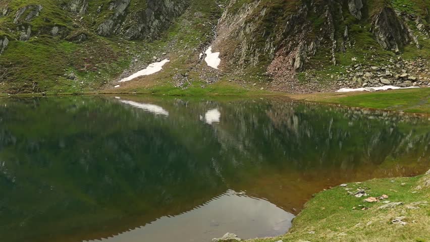A small mountainous lake surrounded by green mountains during the daytime