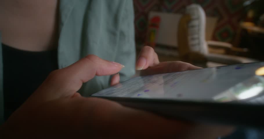 A woman sends text messages on a mobile phone sitting indoors. Close-up of her hands, an unrecognizable person