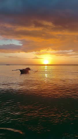 Dreamy summer sunset view of the ambient motion of the gentle waves cradling a moored bangka, a native watercraft of the Philippines 
