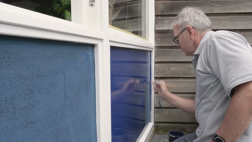 Mature grey haired man painting the outside walls