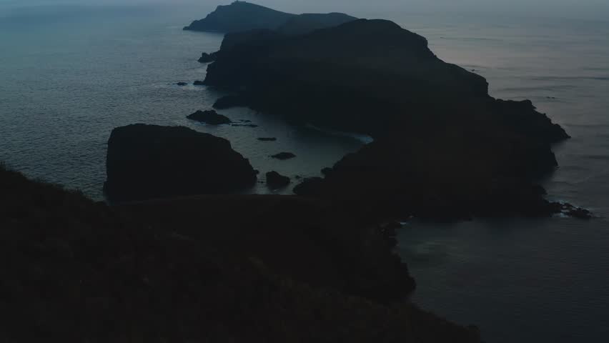 A drone view over dark massive cliffs on a lake coast during sunset