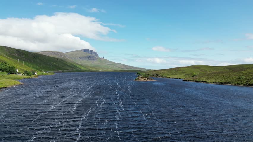 A landscape aerial scene over blue lake with green hills and blue cloudy sky on the horizon