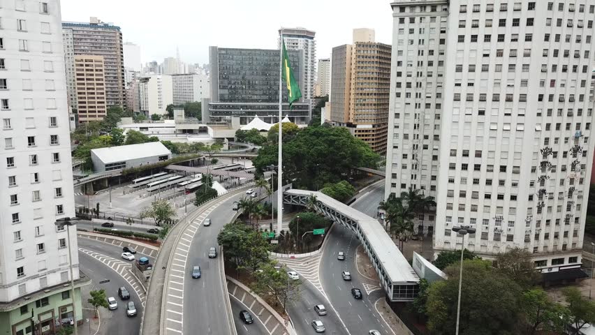 Drone view of downtown São Paulo, showing tall buildings, the Brazilian flag, and the urban landscape.